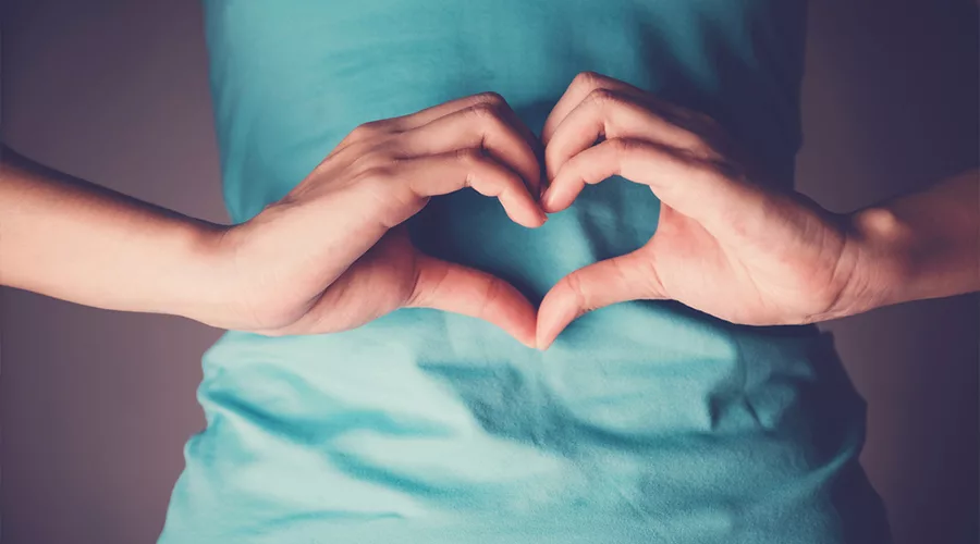 Woman hands making a heart shape on her stomach